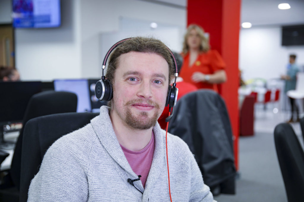 Swansea employee with headset on smiling at desk.