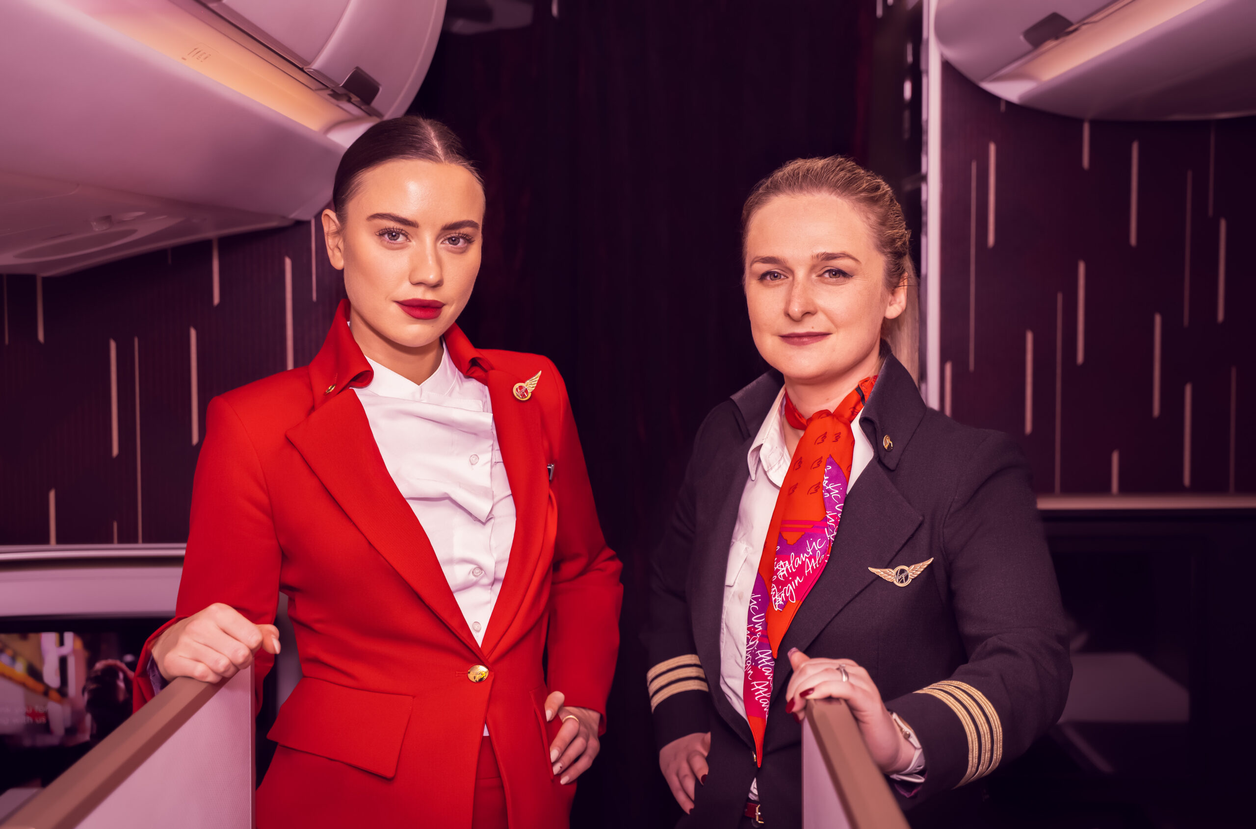 Two female Virgin Atlantic crew members in uniform, posing inside an aircraft