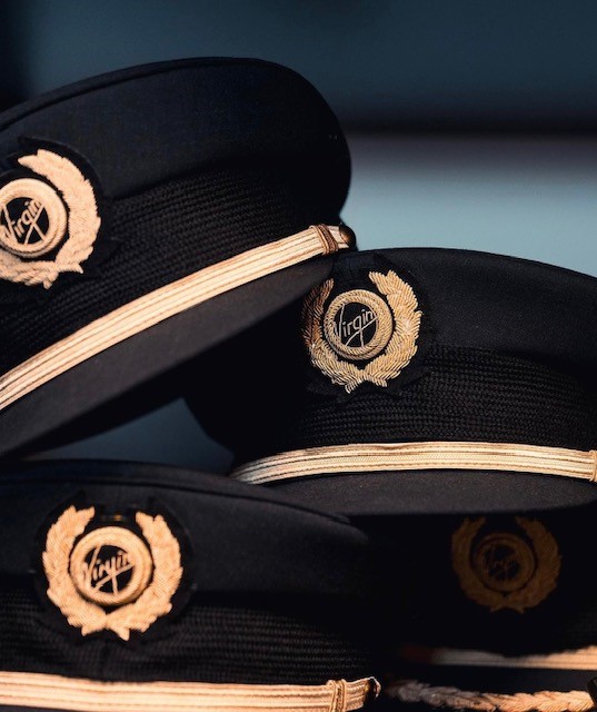 Four black hats with gold trim displayed together, featuring the Virgin Atlantic logo