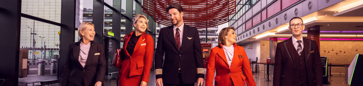 Five crew members, including pilots and flight attendants in uniform, walk together inside a modern airport terminal.