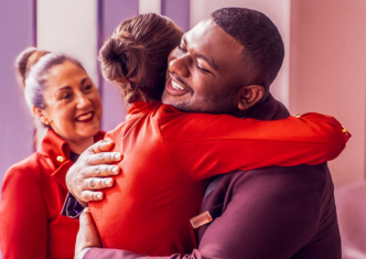 Three Virgin Atlantic crew members smiling as two colleagues greet each other with a hug