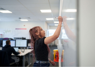 A woman writing on a whiteboard in a modern office